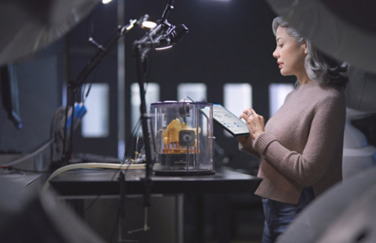 A woman is reading content on a tablet while standing in a lab type room.