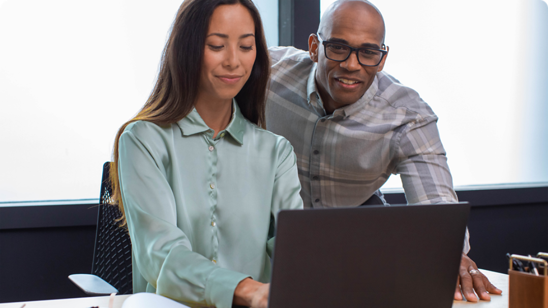 Two people collaborating on a laptop in an office setting.