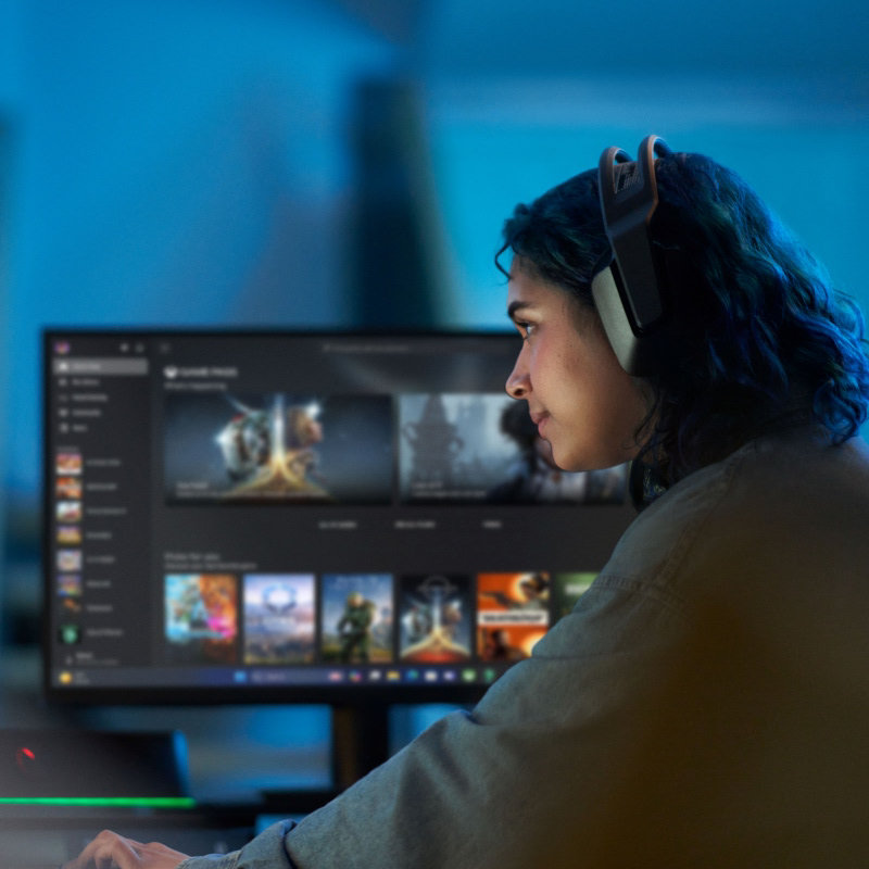 A woman wearing headphones looking at a large monitor displaying PC games