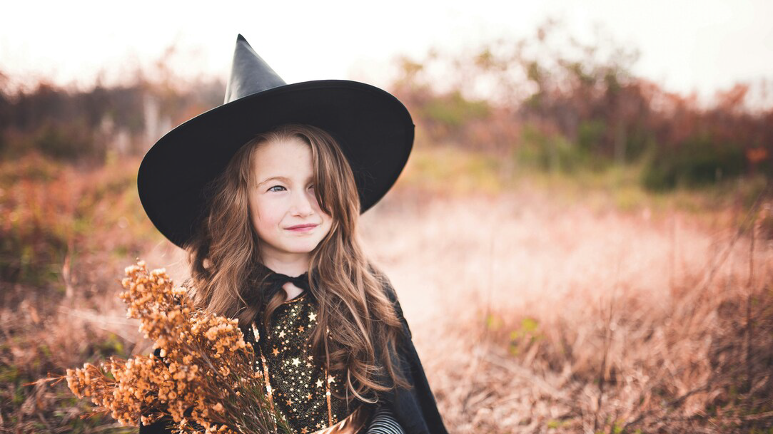 Girl wearing a black witch costume holding a brown plant in a field