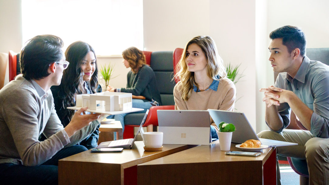 Group of people sitting at a table and using Surface devices