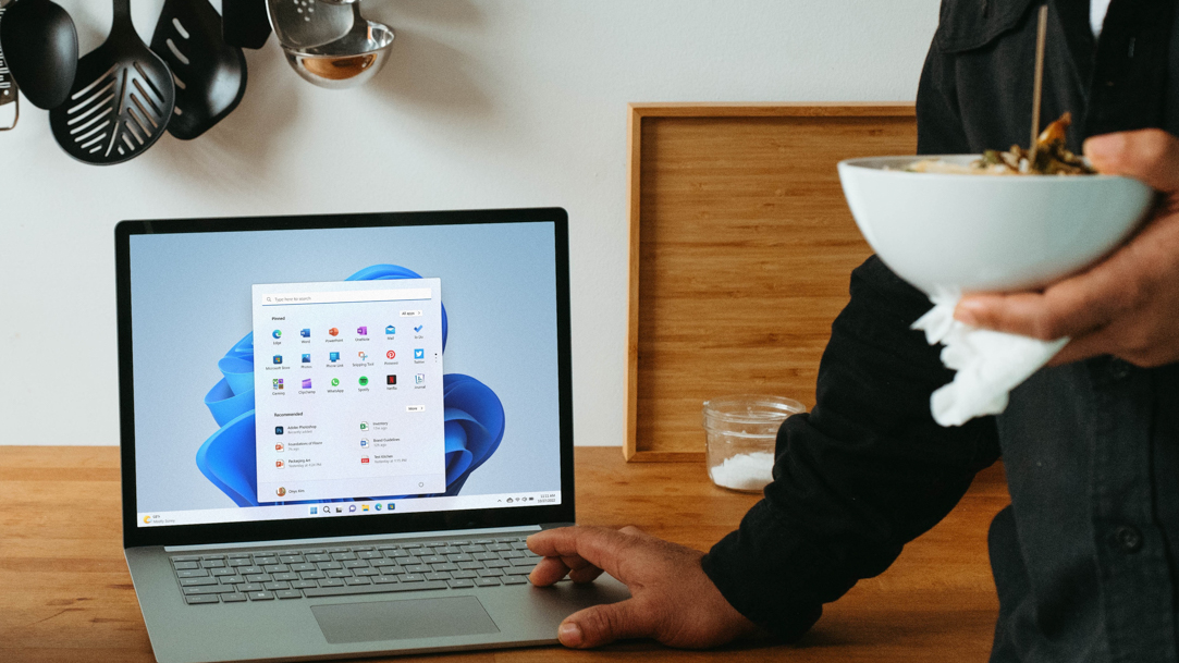 Man holding a bowl of food while looking at his computer