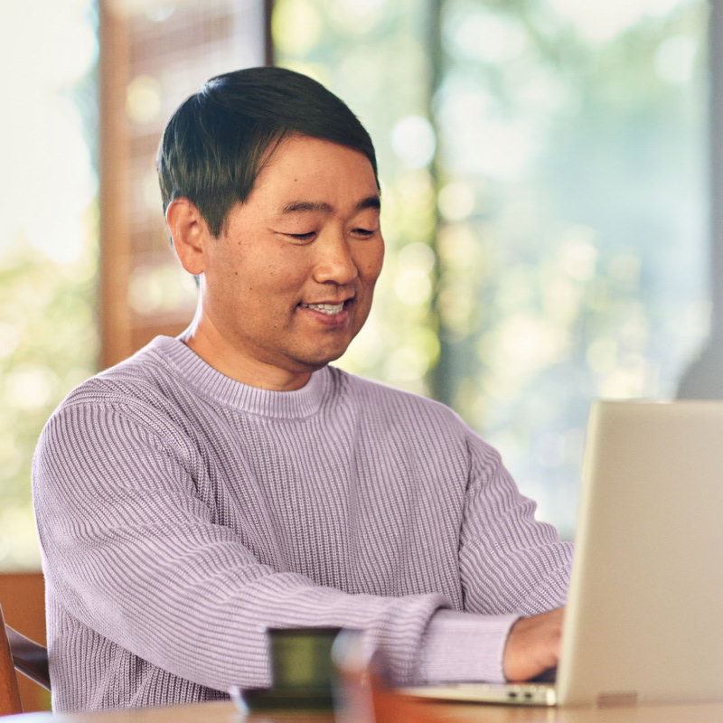 A smiling man sitting at a desk and working on an open laptop