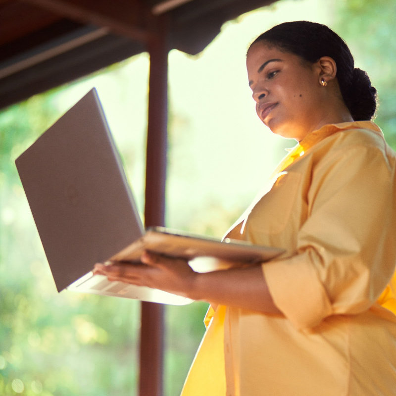 A woman standing and working on an open laptop