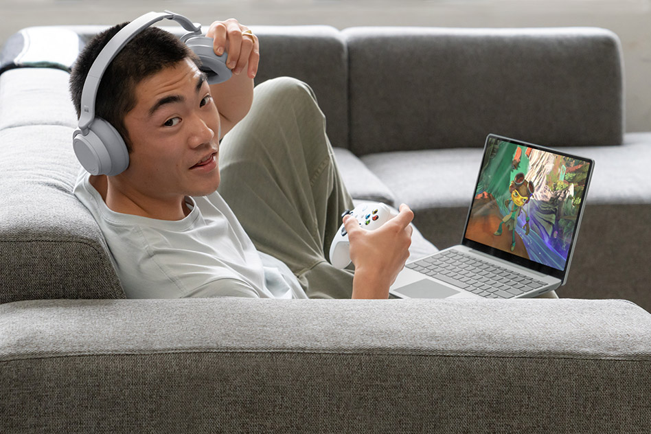 A man plays Xbox games on his Surface Laptop while sitting on the couch.