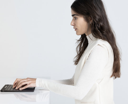 An image of a woman sitting at a desk typing on a keyboard, with the Surface Pro device disconnected from the keyboard and on a stand.