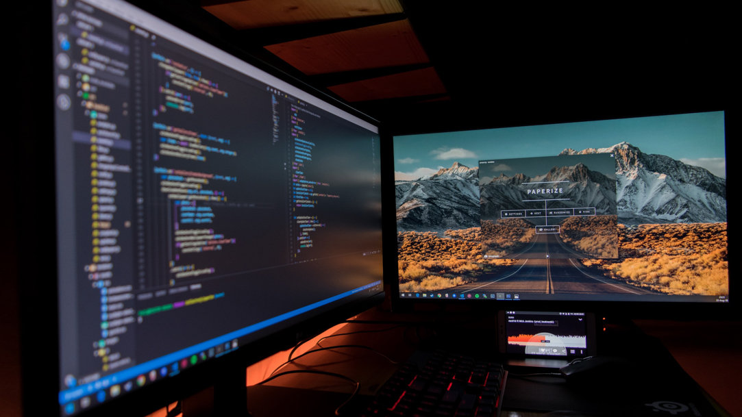 Two monitors with multiple floating windows open in a dark room