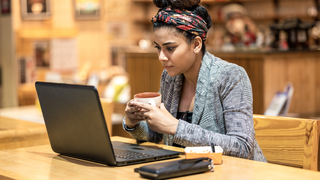 Woman looking at laptop while holding coffee