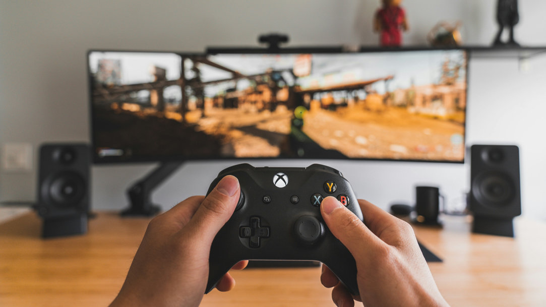 person holding black Xbox controller in front of computer monitors