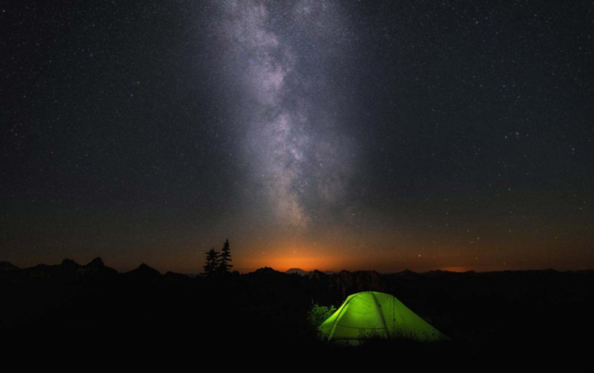 An illuminated tent sits under the milky way.