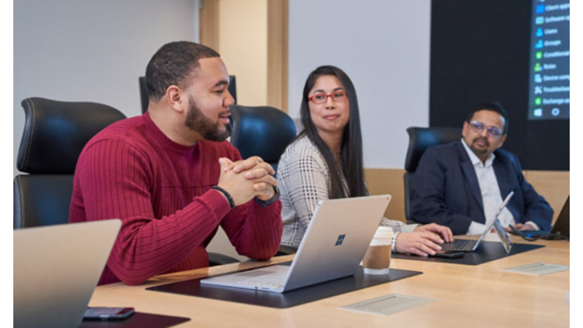 Group of people at a conference table with laptops who appear to be having a healthy and positive discussion or meeting