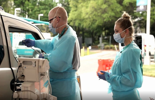 Two people in personal protective equipment providing medical service to someone in an vehicle