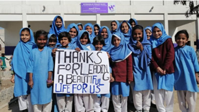 A group of children in school uniforms holds a sign that reads, “Thanks for leading a beautiful life for us.”