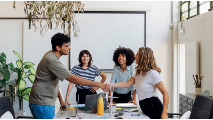 Coworkers smiling and shaking hands in an office meeting.