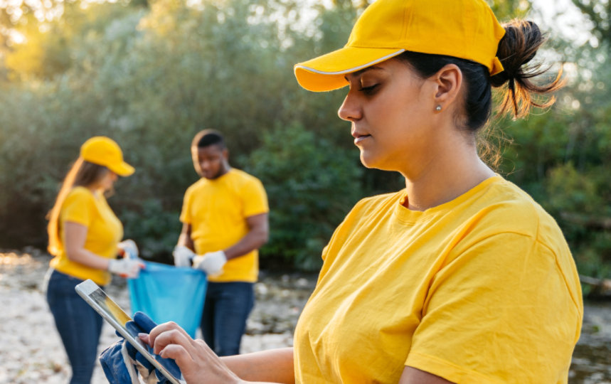 Four volunteers dressed in yellow picking up trash at a riverbank.