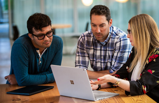 Three people seated around a laptop having a discussion