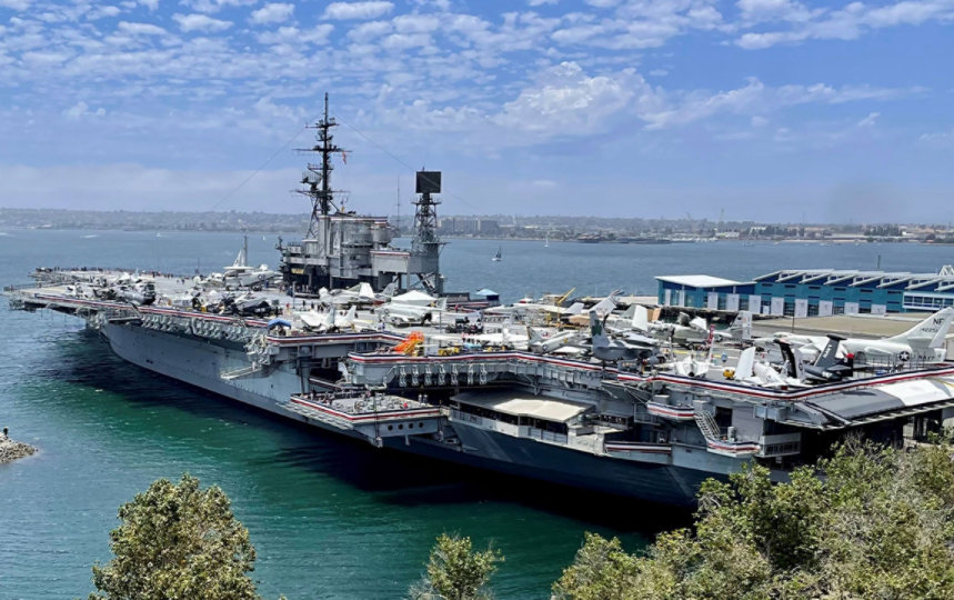 USS Midway, a large aircraft carrier with a flat deck, anchored in calm waters.