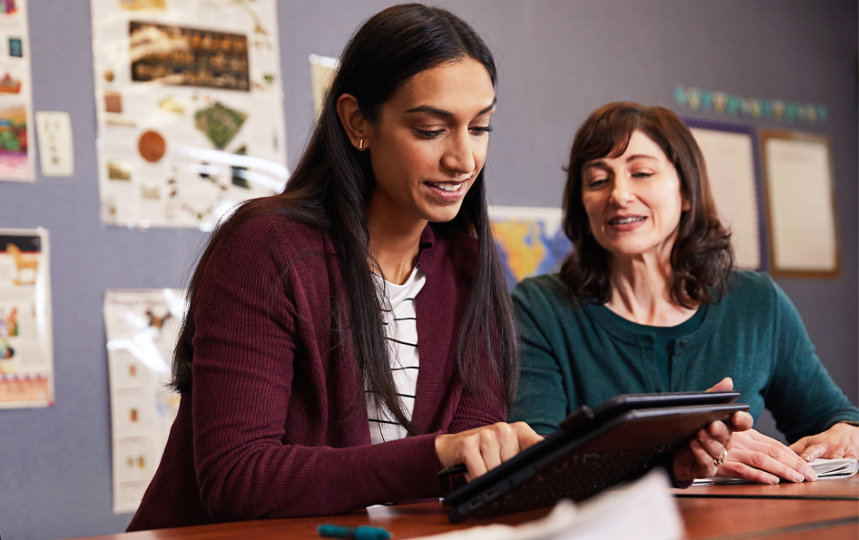 Two women, in a classroom collaborating on a surface tablet.