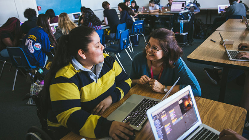 A TEALS volunteer works with a female student in a computer science class.