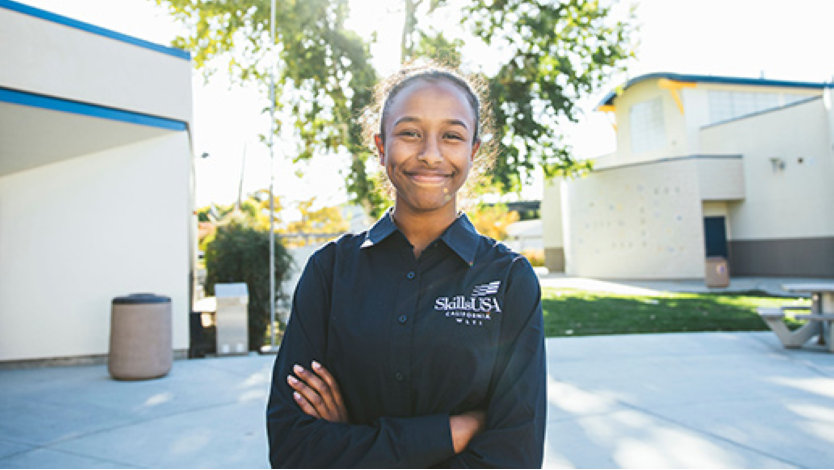 Female high school computer science teacher posing with a smile in a school courtyard 