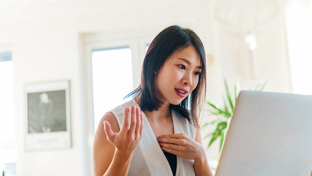 Woman sitting at desk looking at a laptop with a quizzical look