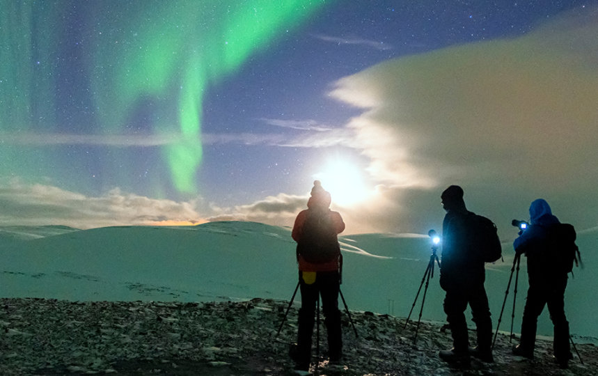 Three people with cameras photographing the northern lights on a cold winter night in Northern Norway.