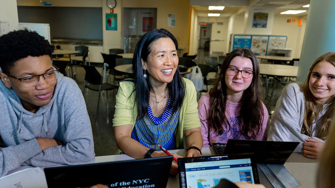 Group of students and a teacher sitting at a table with computers