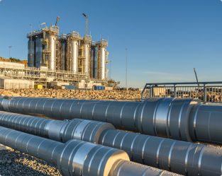 An industrial gas processing plant with large storage tanks and pipelines, located by a rocky area under a clear blue sky.