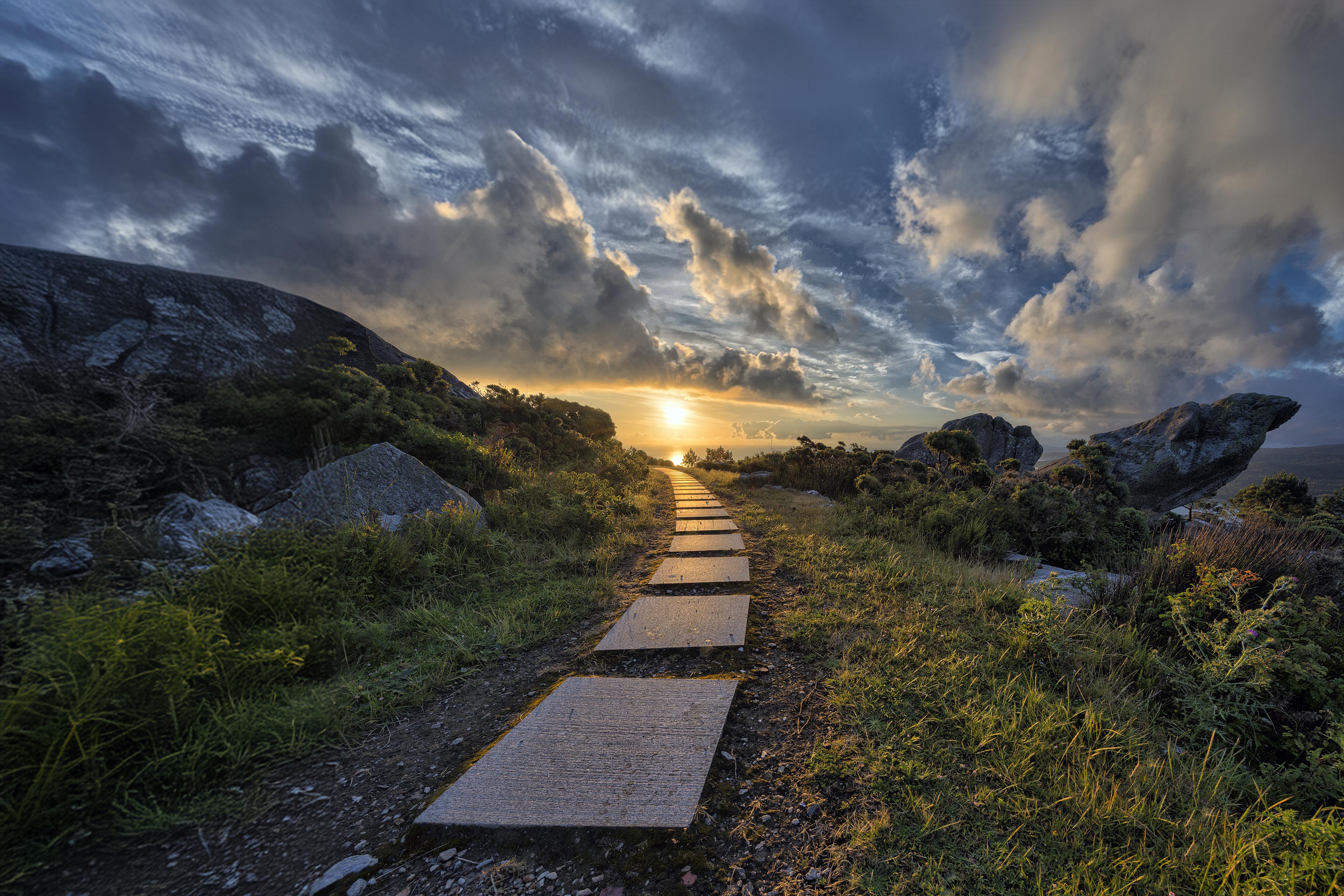 A path leading to sun at sunset with a cloudy sky