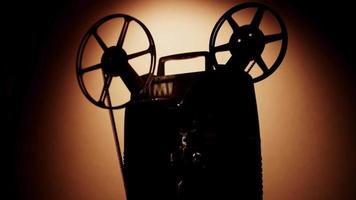 Side view of a silhouette of person turning on and turnin off a 8mm movie projector with film reels spinning in 4K video