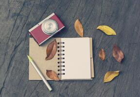 Retro camera, open blank book with dry leaf on wood background photo