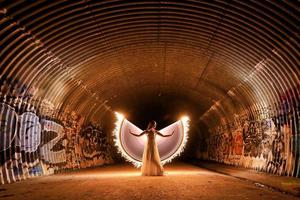 Posando mujer pintada de luz con alas en un túnel de alcantarillado foto