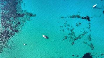 Top view of a white sand beach full of people enjoying a hot sunny day nearby several trees on the field and cliffs with boats sailing on the sea video