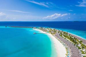 Aerial view of Maldives island, luxury water villas resort and wooden pier. Stunning sky and ocean lagoon beach. Summer vacation holiday and travel concept. Paradise aerial landscape panorama photo