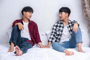 Two dear young men were sitting on the bed, holding hands and looking at each other. photo