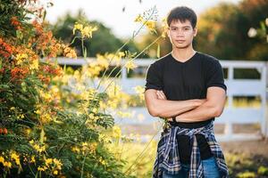 The male traveler wears a black shirt and stands in a flower garden. photo