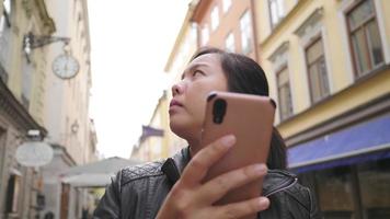 mulher asiática em pé e usando smartphone para ver o mapa da cidade, se perdendo na pequena cidade, saindo para passear na rua na suécia. viajar para o exterior em férias prolongadas video