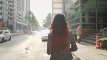 seguindo a bela jovem turista vestindo jaqueta preta e bolsa, aproveitando a luz do sol na cidade grande, andando na rua. video