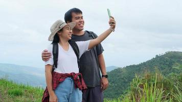 mochileiros de viajantes de homem e mulher usam telefones celulares para tirar selfies no fundo da montanha. casal de caminhadas relaxantes na natureza de férias. video