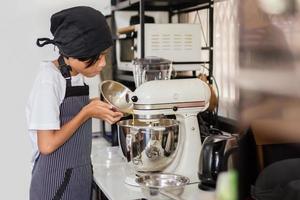 Young boy pouring egg yolk into electric mixer bowl. photo