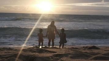 feliz família asiática de mãe e filhas se divertindo jogando na praia durante as férias de verão ao pôr do sol. viagem em família de verão para a praia. conceito de viagens e férias. video