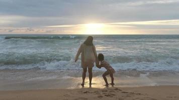 feliz família asiática de mãe e filha se divertindo jogando na praia durante as férias de verão ao pôr do sol. viagem em família de verão para a praia. conceito de viagens e férias. video