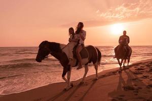 The family spends time with their children while riding horses together on a sandy beach. Selective focus photo