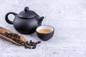 Hot tea in black teapot and cups and dry tea leaves over bright gray cement background, close up, copy space design concept. photo