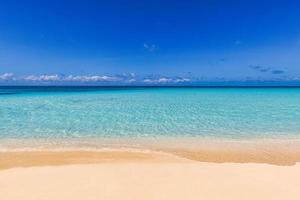 Closeup of sand on beach and blue summer sky. Panoramic beach landscape. Empty tropical beach and seascape. Sunny blue sky, soft sand, calmness, tranquil relaxing sunlight, summer mood. Waves shore photo