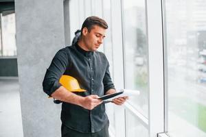 Male worker or engineer with yellow hard hat standing indoors with notepad photo