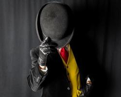 Portrait of Man in Dark Suit and Yellow Vest and Red Tie Holding Bowler Hat Over His Face photo