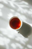 White cup of tea on abstract background of natural curtain shadow falling on white table. photo