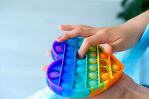 Child playing with rainbow pop it fidget toy. Push bubble fidget sensory toy - washable and reusable silicon stress relief toy. A little girl plays with an anti-stress toy. photo