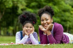 africano americano madre y joven hija son acostado abajo después teniendo un verano picnic en el público parque para fin de semana ocio y felicidad concepto foto